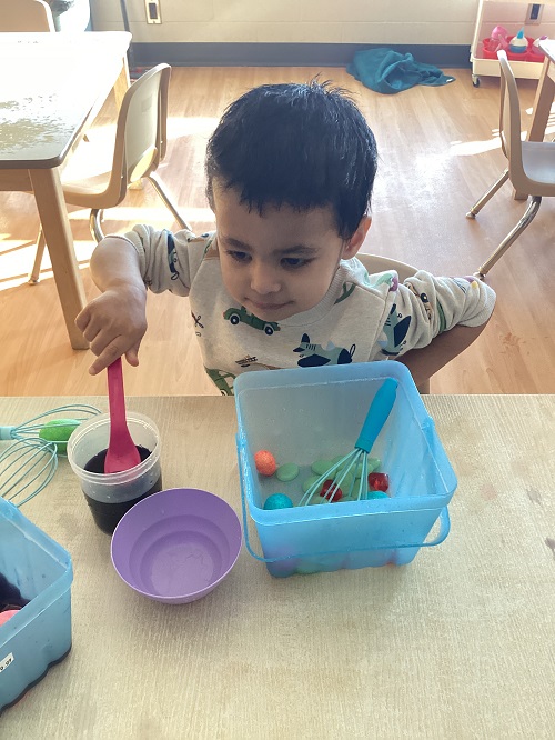A toddler holding a spoon in a container with water