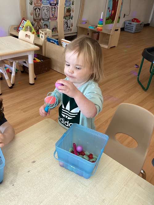 A toddler child placing plastic eggs into a whisk
