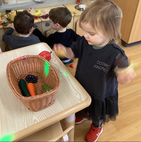 A toddler looking at play food in a basket