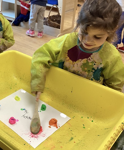 A child using a wooden spoon to create colour splats on paper