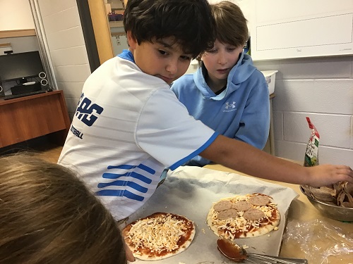 Two school aged children making pizzas