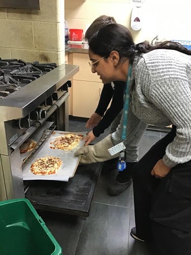 Educator and school aged child putting pizza in the oven