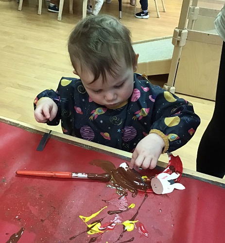 A toddler painting with brown paint